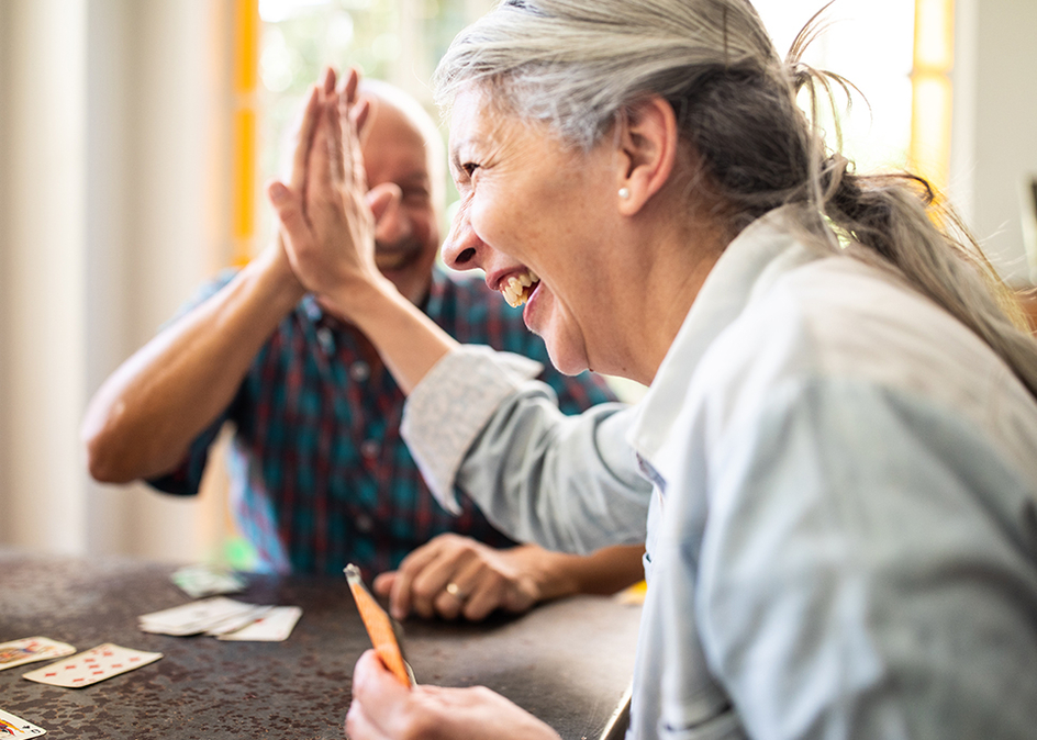 Two seniors playing a card game and giving each other a high five.