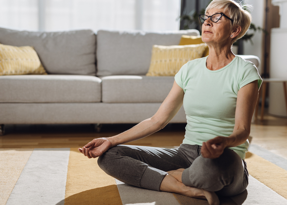 Senior woman doing the lotus yoga position in her living room.