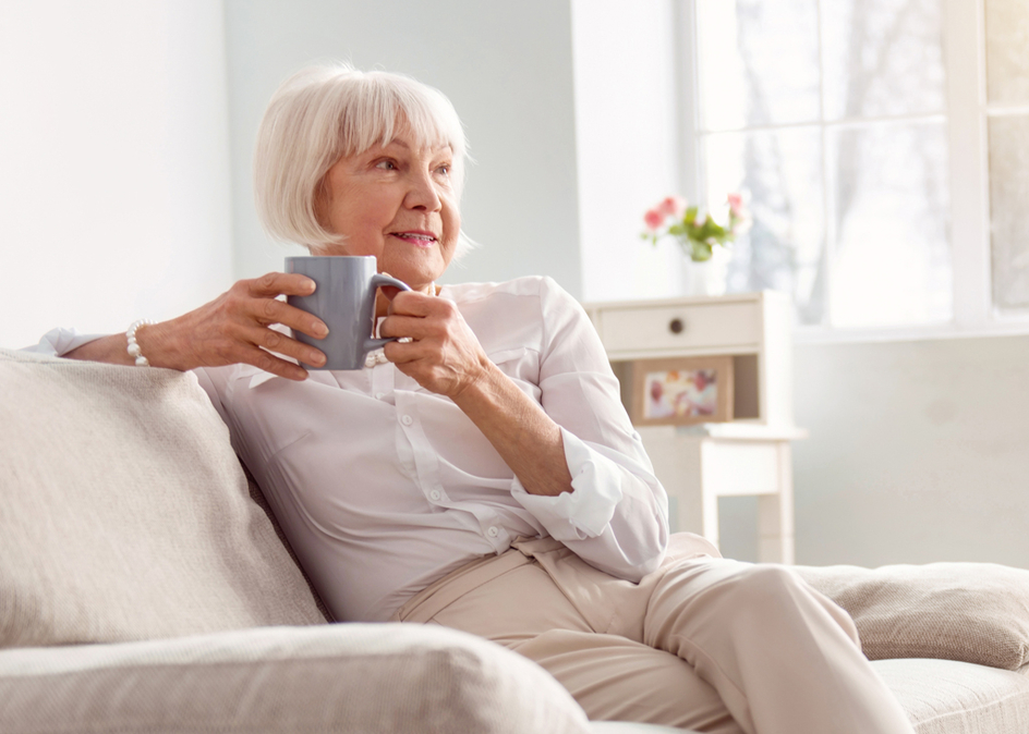 Senior woman sitting on the couch in her living room, drinking coffee