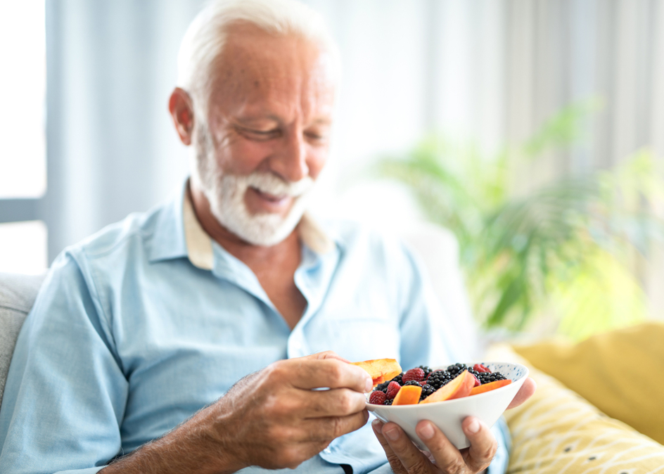 Happy senior man eating healthy fruits while relaxing on sofa at home.