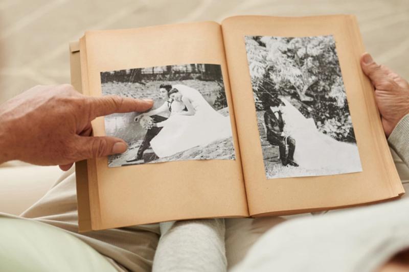 A photo album sits in the lap of a senior who points at the photos.
